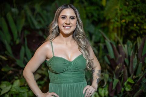 Alt text: formanda posando com vestido verde e sorrindo com folhagens verdes de fundo'