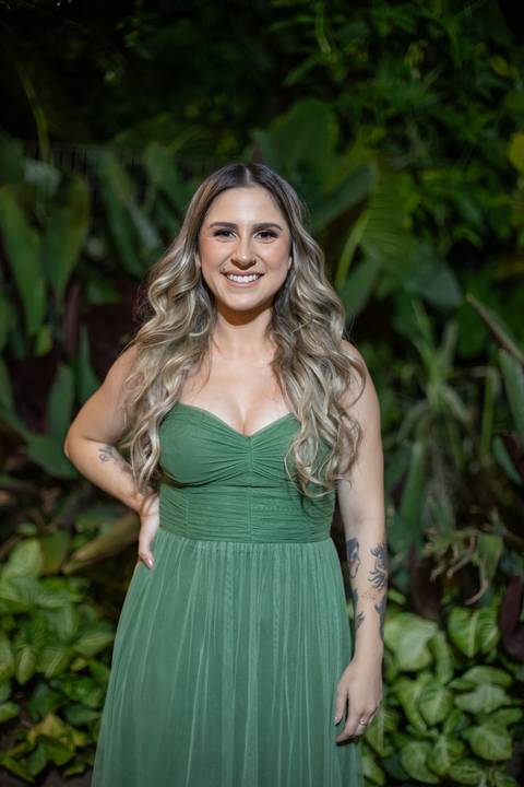 Alt text: formanda posando com vestido verde e sorrindo com folhagens verdes de fundo'