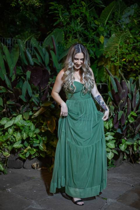 Alt text: formanda posando com vestido verde e sorrindo com folhagens verdes de fundo'