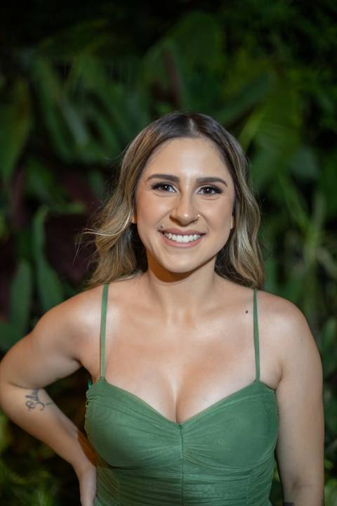 Alt text: formanda posando com vestido verde e sorrindo com folhagens verdes de fundo'