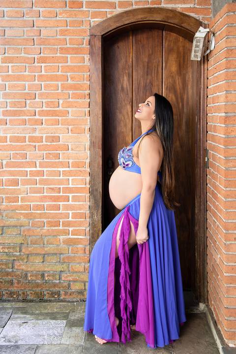 Foto da Grávida Olhando Para o Céu  Em Frente à uma Parede de Tijolinhos Usando um Top e Saia Longa No Estúdio Jardim Guedala em São Paulo, Foto Feita Pela Priscila Felix Fotógrafa de Família, Casamento e Ensaios '
