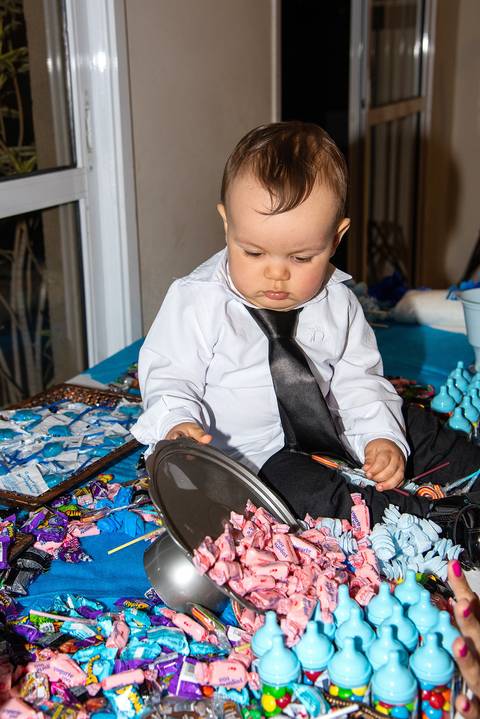 Foto do Aniversariante Sentado na Mesa de Doces Derrubando a Bandeja de Balas Na Vila Andrade - SP. Foto por Priscila Felix, fotógrafa de família, ensaios, eventos e casamentos.'