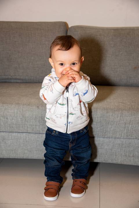 Foto do Aniversariante Em Pé Sorrindo e Mordendo as Mãos Na Vila Andrade - SP. Foto por Priscila Felix, fotógrafa de família, ensaios, eventos e casamentos.'