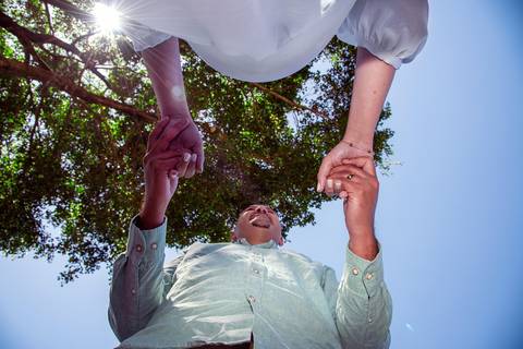 Foto do Casal de Mãos Dadas Vista de Baixo Focando na Barriga e No Céu Azul No Restaurante Velhão Na Cantareira em São Paulo, Foto Feita Pela Priscila Felix Fotógrafa de Família, Casamento e Ensaios '