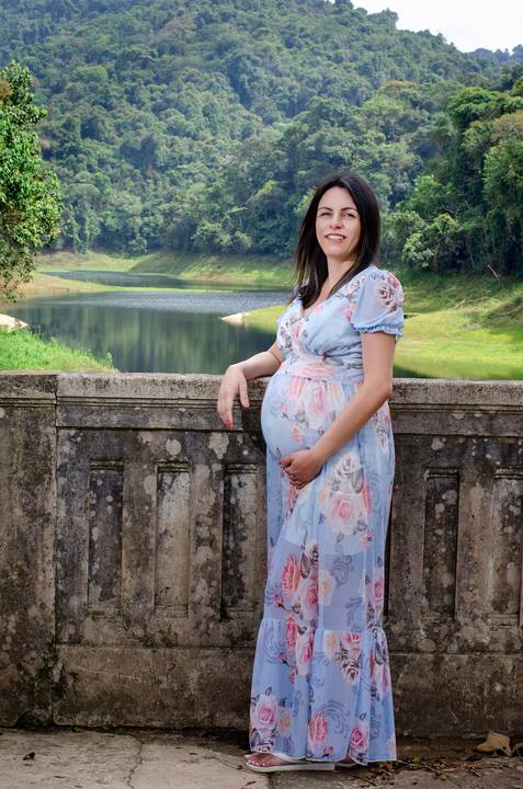 Foto da Mãe de Vestido Azul Clarinho Com As Mãos na Barriga E Ao Fundo As Águas da Represa No Núcleo Engordador Na Cantareira em São Paulo, Foto Feita Pela Priscila Felix Fotógrafa de Família, Casamento e Ensaios '