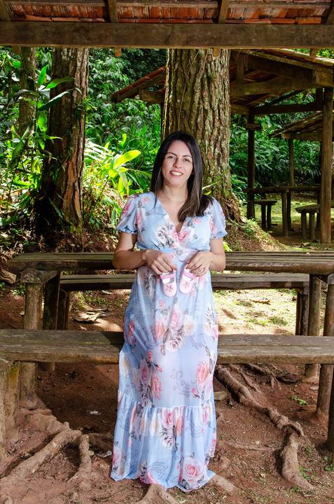 Foto da Mãe de Vestido Azul Clarinho Sentada Com O Sapatinho da Bebê Na Barriga No Núcleo Engordador Na Cantareira em São Paulo, Foto Feita Pela Priscila Felix Fotógrafa de Família, Casamento e Ensaios '