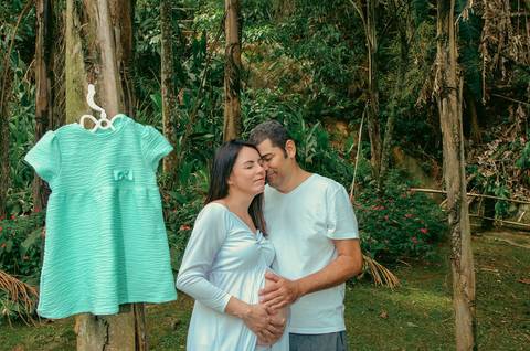 Foto do Casal de Rosto Colado, Olhos Fechados Ao Fundo e Na Frente o Vestidinho Verde da Bebe Pendurado na Árvore No Núcleo Engordador Na Cantareira em São Paulo, Foto Feita Pela Priscila Felix Fotógrafa de Família, Casamento e Ensaios '