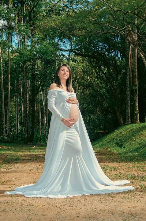 Foto da Mãe Usando Um Vestido Longo Branco Com a Barriga de Fora Olhando Para O Céu Azul e Ao Fundo Um Corredor de Árvores No Núcleo Engordador Na Cantareira em São Paulo, Foto Feita Pela Priscila Felix Fotógrafa de Família, Casamento e Ensaios '