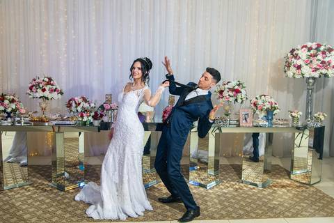Fotografia dos Noivos Brincando em Frente à Mesa do Bolo Ela Puxando a Gravata do Noivo e Ele Fingindo Cair No Buffet Europa em Guarulhos SP Feita por Priscila Felix Fotógrafa de Casamentos, Ensaios e Família'