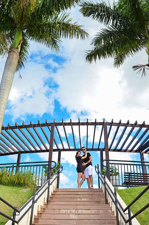 Foto dos Pais Se Abraçando no Topo da Escadaria Com Coqueiros nas Laterais e Um Céu Incrivelmente Azul No Mirante de Guararema - SP, Foto Feita Pela Priscila Felix Fotógrafa de Família, Casamento e Ensaios '