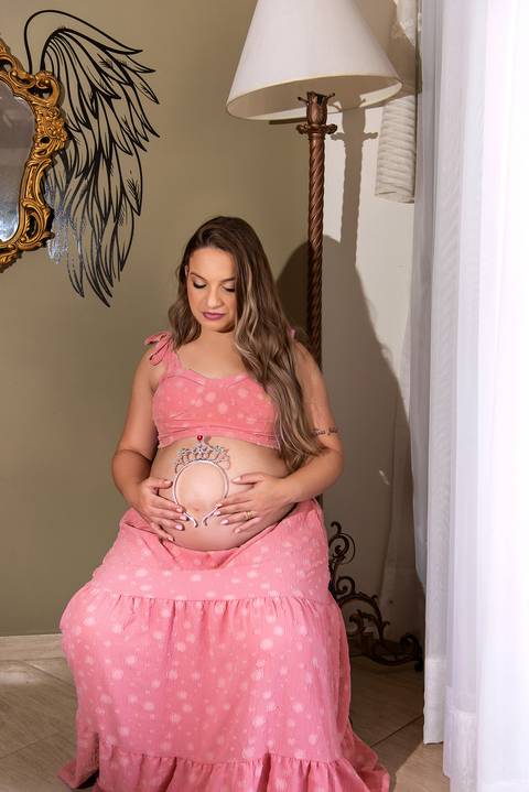 Foto da Mãe Sentada Segurando um Arquinho na Barriga Usando Uma Saia Longa e Um Top Cor de Rosa em São Paulo - SP, Foto Feita Pela Priscila Felix, Fotógrafa de Família, Casamento e Ensaios '