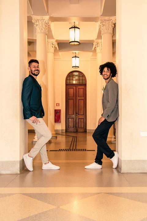Foto do Casal De Frente Um Pro Outro Com os Pés Apoiados na Parede Ao Fundo Um Corredor Com Uma Porta de Madeira Na Estação da Luz em São Paulo - SP, Foto Feita Pela Priscila Felix Fotógrafa de Família, Casamento e Ensaios '