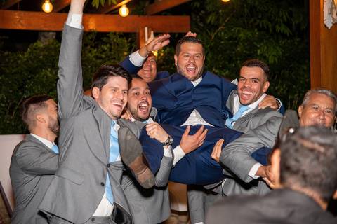 Fotografia do Noivo Sendo Jogado Pra Cima Pelos Padrinhos Em Frente Ao Deck Iluminado Em Mairiporã SP Feita por Priscila Felix Fotógrafa de Casamentos, Ensaios e Família'