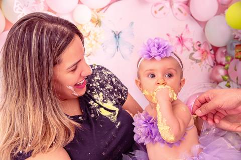 Fotografia da Bebê Comendo o Bolo No Colo da Mãe Já Toda Suja de Bolo no Estúdio Com Cenário Rosa Com Bexigas Personalizadas em SP Feita por Priscila Felix Fotógrafa de Casamentos, Ensaios e Família'