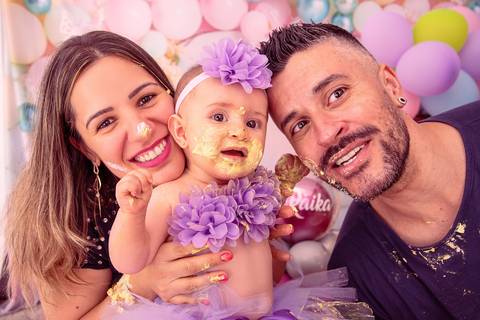 Fotografia da Bebê Com os Pais Todos Sujos de Bolo no Estúdio Com Cenário Rosa Com Bexigas Personalizadas em SP Feita por Priscila Felix Fotógrafa de Casamentos, Ensaios e Família'