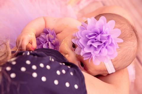 Fotografia da Bebê Sendo Amamentada Pela Mãe Segurando o Dedinho Dela e Olhando Com Atenção Estúdio Com Cenário Rosa Com Bexigas Personalizadas em SP Feita por Priscila Felix Fotógrafa de Casamentos, Ensaios e Família'