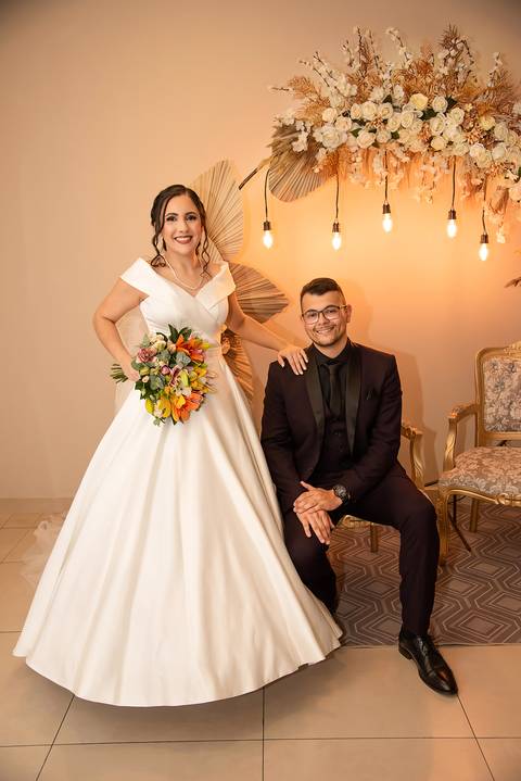 Fotografia do Noivo Sentado e a Noiva Em Pé Ao Lado Com a Mão em Seu Ombro em Guarulhos SP Feita por Priscila Felix Fotógrafa de Casamentos, Ensaios e Família'