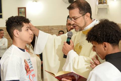 Fotografia do Padre Passando Óleo na Testa Do Crismado Fazendo a Cruz Na Igreja São José em São Paulo, SP Feita por Priscila Felix Fotógrafa de Casamentos, Ensaios e Família'