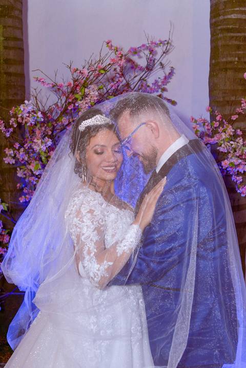 Fotografia dos Noivos Sob o Véu da Noiva Sorrindo Com Uma Luz Roxa Iluminando Por Trás No Jardim em Mansão Pimenta Nativa Salão de Festas no Tatuapé - SP Feita por Priscila Felix Fotógrafa de Casamentos, Ensaios e Família'
