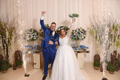 Fotografia dos Noivos Celebrando Com as Mãos Para Cima e Fogos de Artifício Saindo Pelas Laterais em Mansão Pimenta Nativa Salão de Festas no Tatuapé - SP Feita por Priscila Felix Fotógrafa de Casamentos, Ensaios e Família'