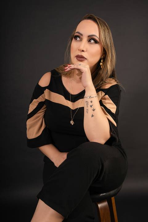 Foto da Modelo No Estúdio Com Fundo Preto Sentada Numa Banqueta Com a Mão Em Frente Ao Queixo Olhando Para o Lado No Estúdio Noma Conecta No Ipiranga em São Paulo - SP, Foto Feita Pela Priscila Felix Fotógrafa de Família, Casamento e Ensaios '