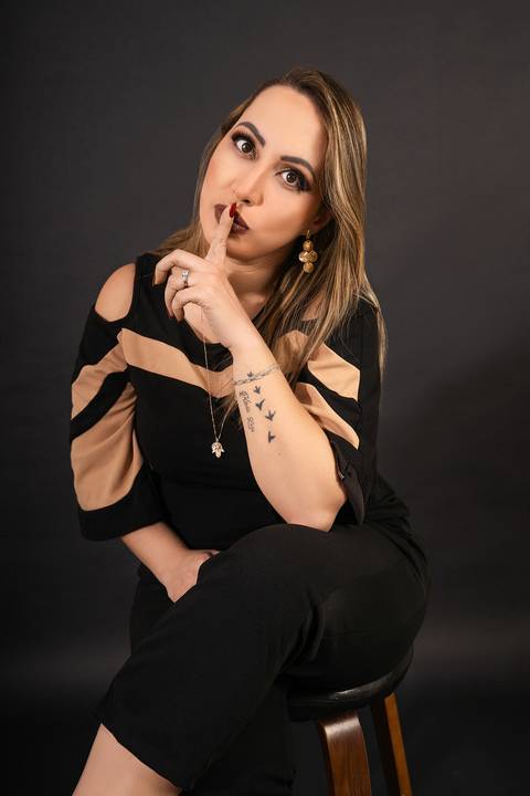 Foto da Modelo No Estúdio Com Fundo Preto Sentada Numa Banqueta Com a Mão Pedindo Silêncio Olhando Para a Frente No Estúdio Noma Conecta No Ipiranga em São Paulo - SP, Foto Feita Pela Priscila Felix Fotógrafa de Família, Casamento e Ensaios '