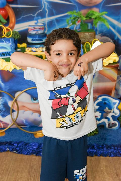 Foto do Aniversariante Em Frente a Mesa do Bolo Mostrando As Tatuagens do Sonic No Dorso das Mãos No Buffet Festas & Cia Na Mooca - SP, Foto Feita Pela Priscila Felix Fotógrafa de Família, Casamentos e Ensaios '