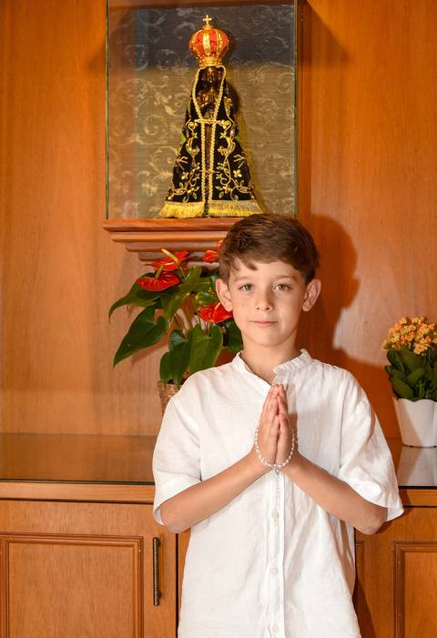 Fotografia do Batizado Segurando o Terço Nas Mãos Em Frente a Imagem de Nossa Senhora Na Igreja Verbo Divino em São Paulo, SP - Feita por Priscila Felix Fotógrafa de Casamentos, Ensaios e Família'