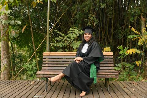 Foto da Formanda Sentada Com As Mãos No Joelho Usando Uma Beca No Parque do Pau D´Alho Em Guararema - SP, Foto Feita Pela Priscila Felix, Fotógrafa de Família, Casamento e Ensaios '