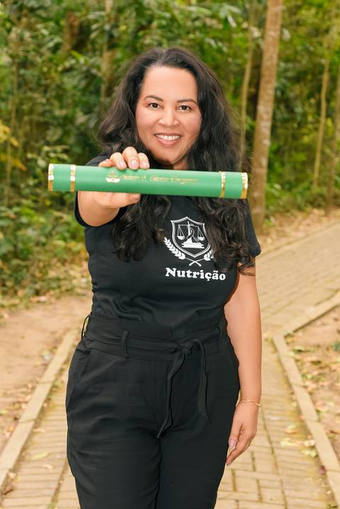 Foto da Formanda Mostrando O Canudo Usando Uma Camiseta Preta Escrita 