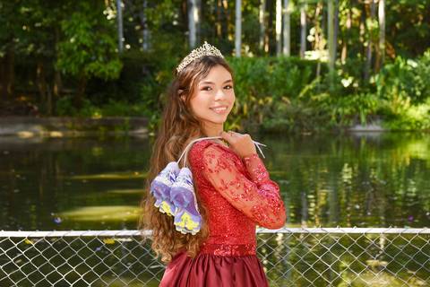 Foto da Debutante Em Frente Ao Lago Usando o Vestido Vermelho, A Coroa E Segurando Uma Chuteira Lilás Nas Costas Pelo Cadarço No Parque da Água Branca Em São Paulo - SP, Foto Feita Pela Priscila Felix Fotógrafa de Família, Casamentos e Ensaios '