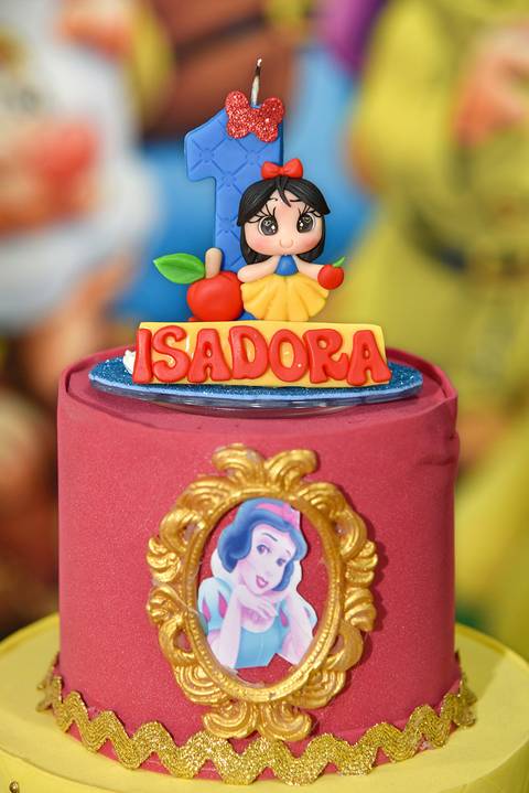 Foto do Bolo Com A Branca de Neve Na Frente E No Topo, a Vela De Numeral Um Azul, O Nome 