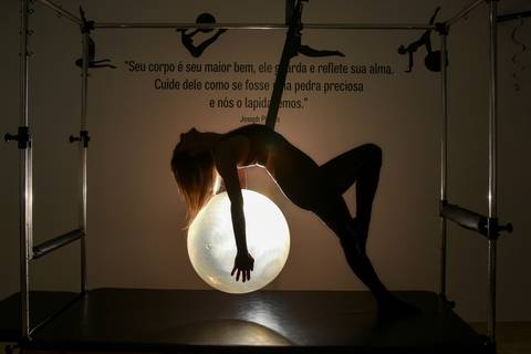 Foto da Silhueta da Modelo Pendurada No Cadillac, Segurando A Bola de Pilates Nas Costas Iluminada, Como Se Fosse a Lua, No Estúdio De Pilates  em São Paulo - SP, Foto Feita Pela Priscila Felix Fotógrafa de Família, Casamento e Ensaios '