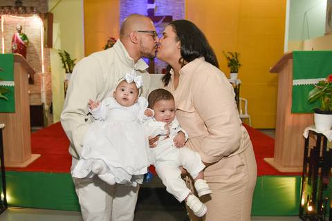 Fotografia Dos Pais Se Beijando Com Os Gêmeos Iogo E Cecília No Colo Na Paróquia São Judas Tadeu em São Paulo, SP Feita por Priscila Felix Fotógrafa de Casamentos, Ensaios e Família'