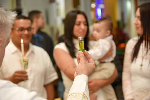 Fotografia Do Padre Mostrando O Óleo Antes de Passar No Peito Do Bernardo Na Paróquia São Judas Tadeu em São Paulo, SP Feita por Priscila Felix Fotógrafa de Casamentos, Ensaios e Família'