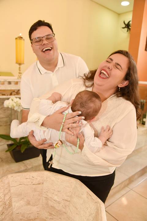 Fotografia Da Mãe Segurando O Rafael No Colo Gargalhando Ao Lado do Pai Na Pia Batismal Na Paróquia Cristo Rei em São Paulo, SP Feita por Priscila Felix Fotógrafa de Casamentos, Ensaios e Família'