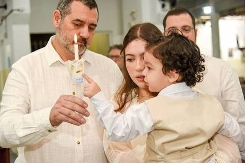 Fotografia Do Theo No Colo Da Madrinha Tentando Pegar A Vela Acesa Na Mão Do Padrinho Na Paróquia São Judas Tadeu em São Paulo, SP Feita por Priscila Felix Fotógrafa de Casamentos, Ensaios e Família'