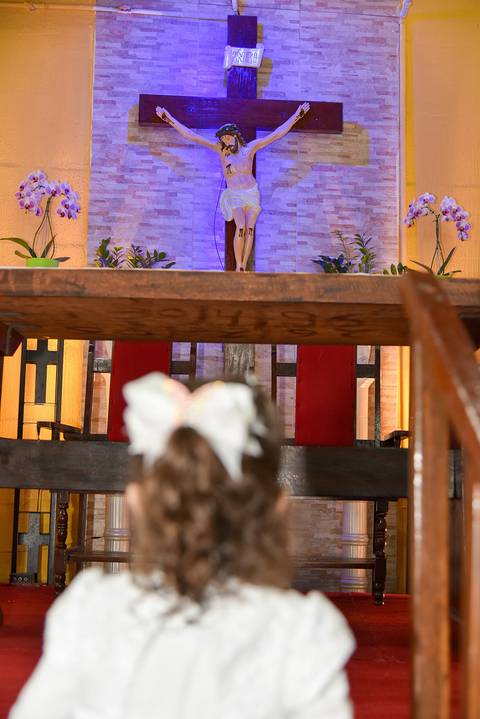 Fotografia Do Cristo No Altar Ao Fundo E A Manuella Ajoelhada De Frente À Ele Desfocada Na Paróquia São Judas Tadeu em São Paulo, SP Feita por Priscila Felix Fotógrafa de Casamentos, Ensaios e Família'