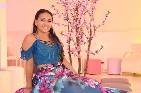 Fotografia da Debutante Sentada Com Top Azul e Saia Longa Florida em Itaquera SP Feita por Priscila Felix Fotógrafa de Casamentos, Ensaios e Família'