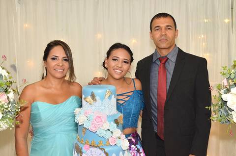 Fotografia da Debutante Com Seus Pais Na Mesa do Bolo Com Top Azul e Saia Longa Florida em Itaquera SP Feita por Priscila Felix Fotógrafa de Casamentos, Ensaios e Família'