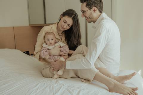 mãe, pai e bebê sentados na cama'