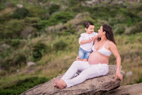 ensaio gestante na praia de grumari, mãe e filho sentados numa pedra com paisagem deslumbrante'