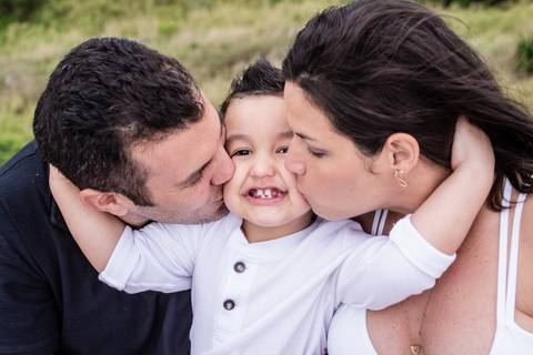 ensaio fotográfico gestante na praia de grumari no rio de janeiro, pai e mãe beijando o filho no rosto ao mesmo tempo!'