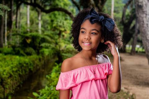 Milena Pinheiro, modelo de cabelo crespo,  fazendo pose com mão no cabelo em ensaio infantil no Jardim Botânico do Rio de Janeiro.'