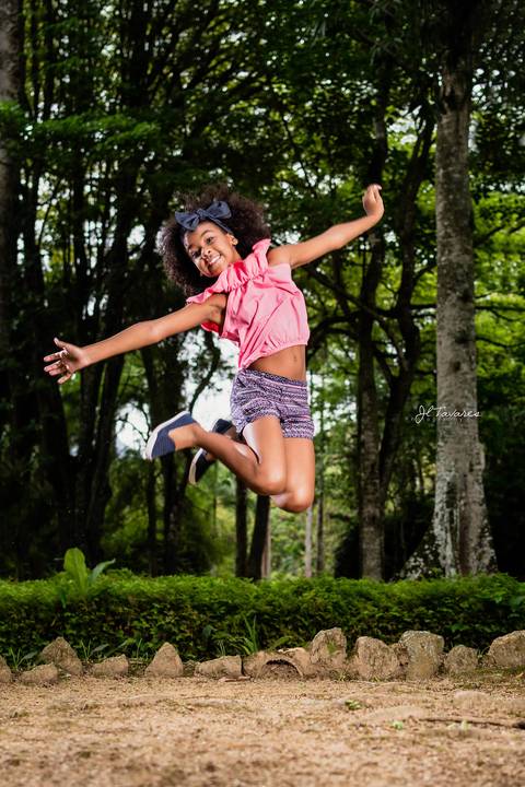 Milena Pinheiro vestindo short estampado azul e rosa com blusa rosa pulando para pulando para ser clicada no ar em seu ensaio infantil.'