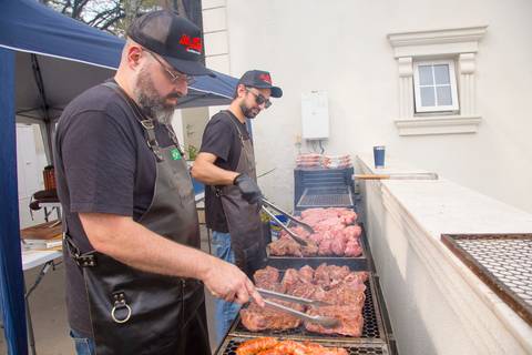 Dois churrasqueiros experientes preparando cortes de carne premium em uma churrasqueira, garantindo o sabor do buffet na festa de 50 anos em uma mansão em São Paulo.'