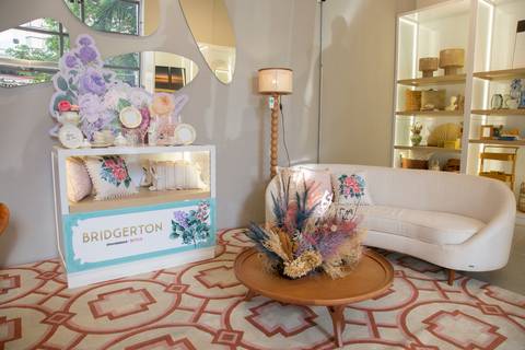 Ambiente decorado na loja Westwing Moema, São Paulo, com sofá clássico, mesa de centro e um móvel com a inscrição 'Bridgerton' e os logotipos da Westwing e Netflix, destacando a parceria.'