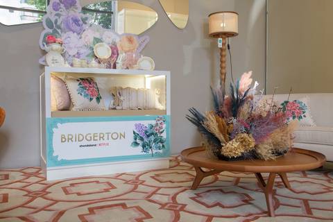 Mesa de centro com decoração temática e um grande painel ao fundo com a identidade visual de Bridgerton, no evento da Westwing + Netflix na loja de Moema, São Paulo.'