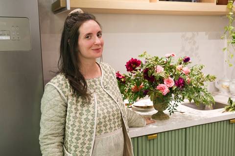 Professora do workshop de arranjo de flores posando com o arranjo floral finalizado, exibindo sua criação no evento Westwing + Netflix Bridgerton em Moema, São Paulo.'