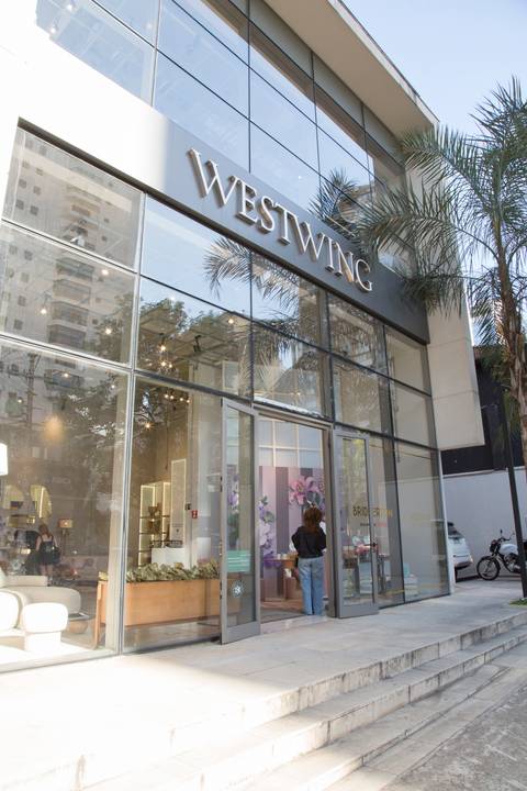Fachada da loja Westwing Moema em São Paulo, com a vitrine exibindo a decoração especial do evento de lançamento das peças Bridgerton, convidando o público.'